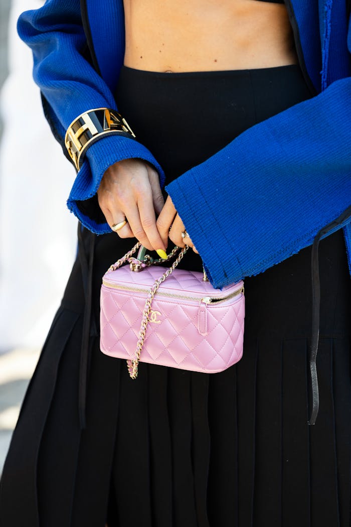 Elegant woman in a stylish blue jacket holding a trendy pink designer bag outdoors.