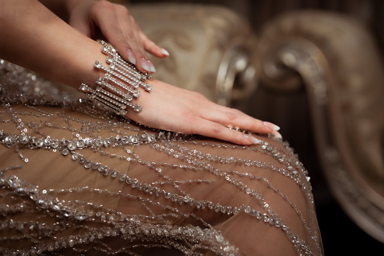 Close-up of a woman's hand with a diamond bracelet on a beaded dress in an elegant setting.